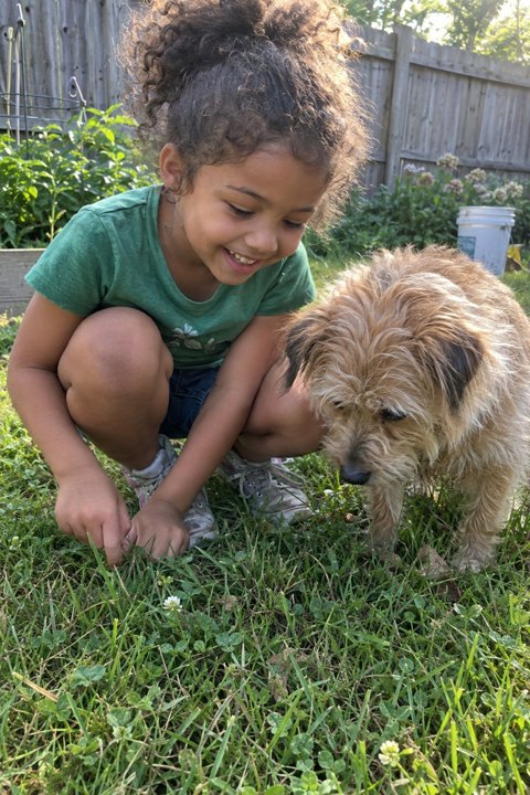 Example photo: Maya crouching in the grass beside her dog Biscuit